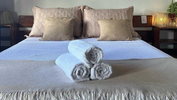 A neatly made bed with a textured blanket, two pillows, and rolled towels. - la bahianita (Itacaré)