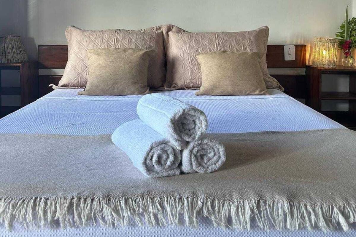 Ein ordentlich bezogenes Bett mit einer gemusterten Decke, zwei Kissen und aufgerollten Handtüchern.