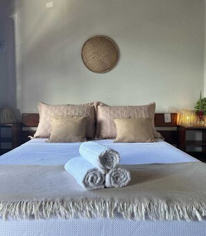 A neatly made bed with a textured blanket, two pillows, and rolled towels. - la bahianita (Itacaré)