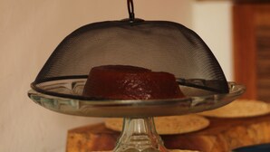 A dessert on a glass stand with a mesh cover, surrounded by woven coasters on a wooden table. - la bahianita (Itacaré)