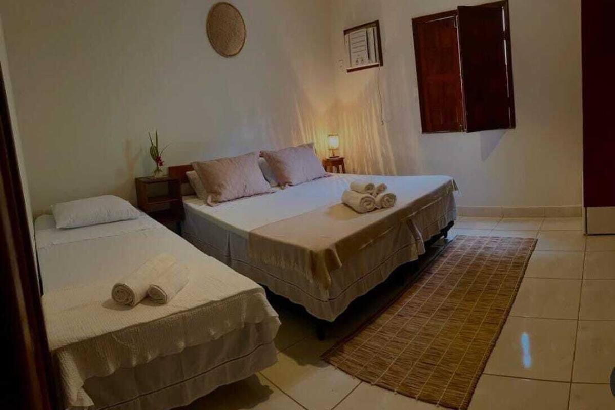 Ein Hotelzimmer mit zwei Betten, einem kleinen Tisch mit Lampe, einer Wanduhr und einem Fenster mit Holzläden.