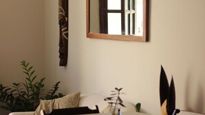 A room with a bed, a dining table, chairs, a mirror, a wall-mounted wooden sculpture, and a hanging hat. - la bahianita (Itacaré)