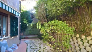 Un sendero de piedra conduce a una casa con puerta verde, un pequeño jardín y un muro de piedra.