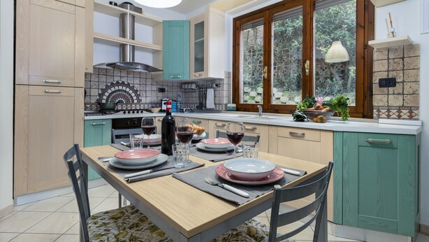 Una cocina moderna con una mesa de comedor dispuesta para cuatro personas, una estufa y un ventanal con vistas al verdor.