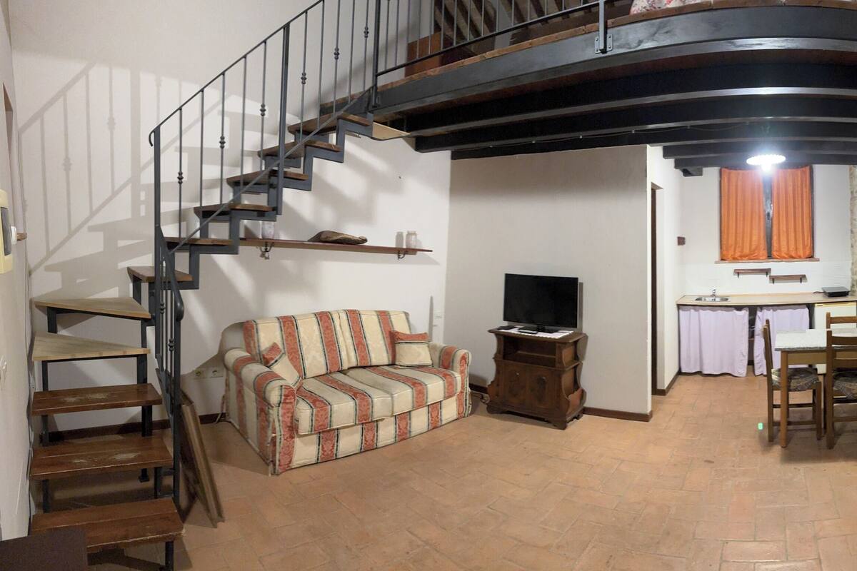 A living room with a sofa, TV, wooden staircase, and a stone wall.
