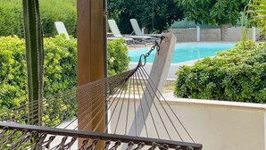 A hammock under a wooden pergola with a view of a swimming pool, lounge chairs, and greenery. - Golden Sand beachfront villa (Castellammare del Golfo)