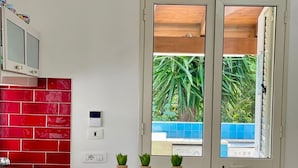 A modern kitchen with red tiles, a wooden countertop, and two white chairs. - Golden Sand beachfront villa (Castellammare del Golfo)