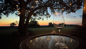 A table with a glass of wine under a tree with string lights, surrounded by a water feature. - Peaceful Texas Retreat w/Gourmet Kitchen, Ranch Views, Optional MasterChef Meals (Lipan)