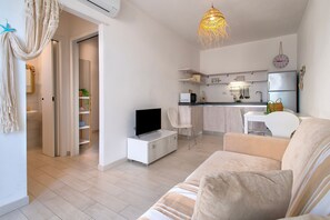 En moderne stue med sofa, fjernsyn og et køkkenområde med køleskab og mikrobølgeovn.