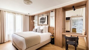 A hotel room with a large bed, a desk, a chair, a mirror, and a bathroom visible through a glass door. - Merveil - Signature Suite - Opera - Bateliere (Paris)
