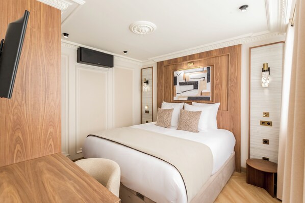 A hotel room with a large bed, a wooden desk, a flat-screen TV mounted on the wall, and a mirror above the bed. - Merveil - Signature Suite - Opera - Bateliere (Paris)