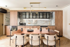 A modern kitchen with a marble backsplash, a dining table with six chairs, and a pendant light fixture.