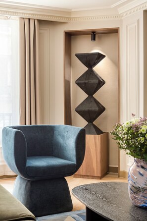 A modern living room with a blue armchair, a geometric wooden sculpture, and a vase with flowers.