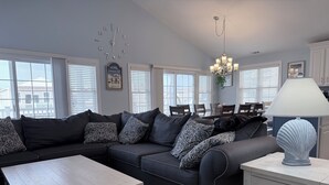 Un salon moderne avec un canapé d’angle, une table basse blanche et un coin repas agrémenté d’un lustre.