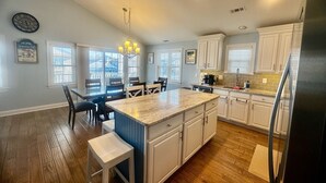Une cuisine moderne avec des meubles blancs, un grand îlot central et un coin repas avec des chaises.