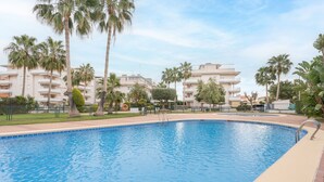 A swimming pool with a clear blue water, surrounded by palm trees and a fence.