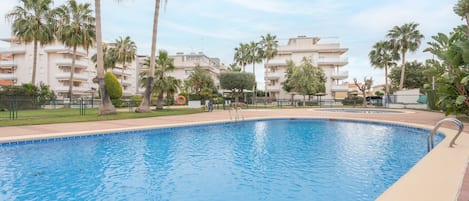 Piscina com água azul cristalina, rodeada por palmeiras e uma cerca.