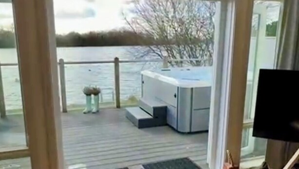 A room with a large glass door leading to a deck with a view of a lake and trees. - Lake Access, Hot Tub, 4+MBed, 3Bth, Landings, Cotswolds Water Park, Sth Cerney (South Cerney)