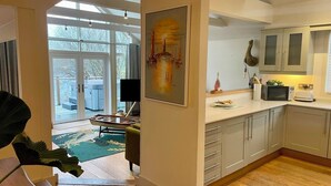 A modern kitchen with white cabinets, a dining area with a table and chairs, and a large window offering a view of the outdoors. - Lake Access, Hot Tub, 4+MBed, 3Bth, Landings, Cotswolds Water Park, Sth Cerney (South Cerney)