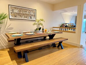 A dining area with a wooden table set for two, a framed liquor bottle illustration on the wall, and a small orchid plant on the table. - Lake Access, Hot Tub, 4+MBed, 3Bth, Landings, Cotswolds Water Park, Sth Cerney (South Cerney)