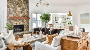 Ein geräumiges Wohnzimmer mit Steinwand, Kamin, einem Essbereich mit Holztisch und einer Küche im Hintergrund.