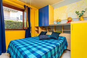 A bedroom with a checkered bedspread, a window with curtains, and a view of a building outside.