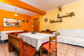 A dining area with a table, chairs, a sofa, and a painting on the wall.