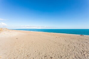 A beach with a clear sky, calm sea, and a few people on the sand.