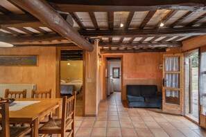 Un intérieur rustique avec une table à manger en bois, des chaises, un canapé et un couloir menant à une chambre.