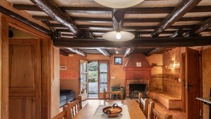 Une table à manger en bois avec des chaises, un chemin de table en dentelle blanche, un luminaire suspendu et une cheminée.