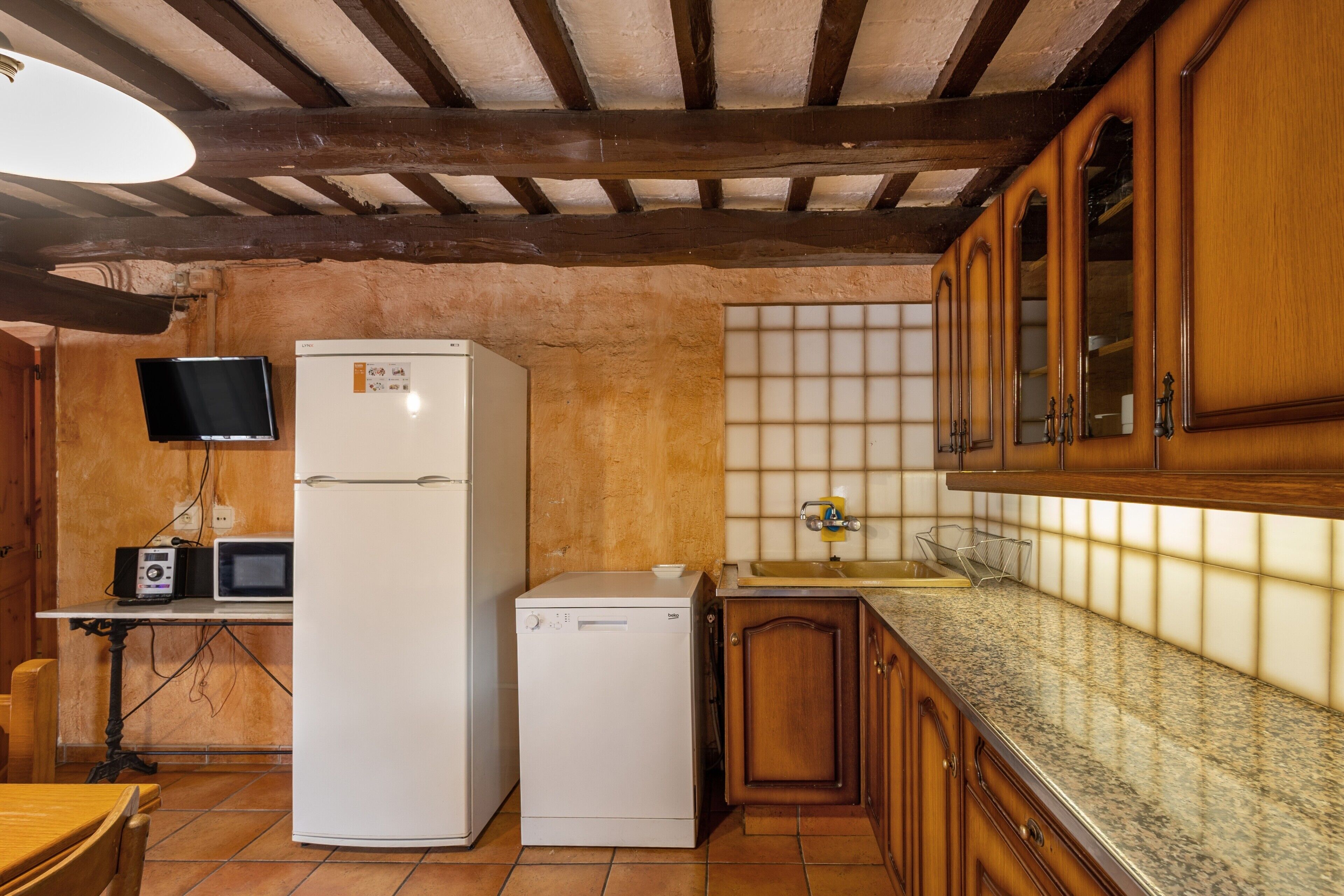 Una cocina con armarios de madera, microondas, refrigerador y salpicadero de azulejos.