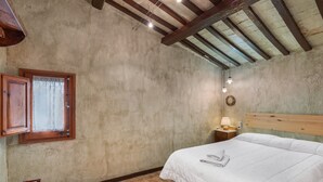 Une chambre à coucher avec une tête de lit en bois, un lit avec une literie blanche, une table de chevet avec une lampe, une fenêtre avec des rideaux et une chaise en bois.