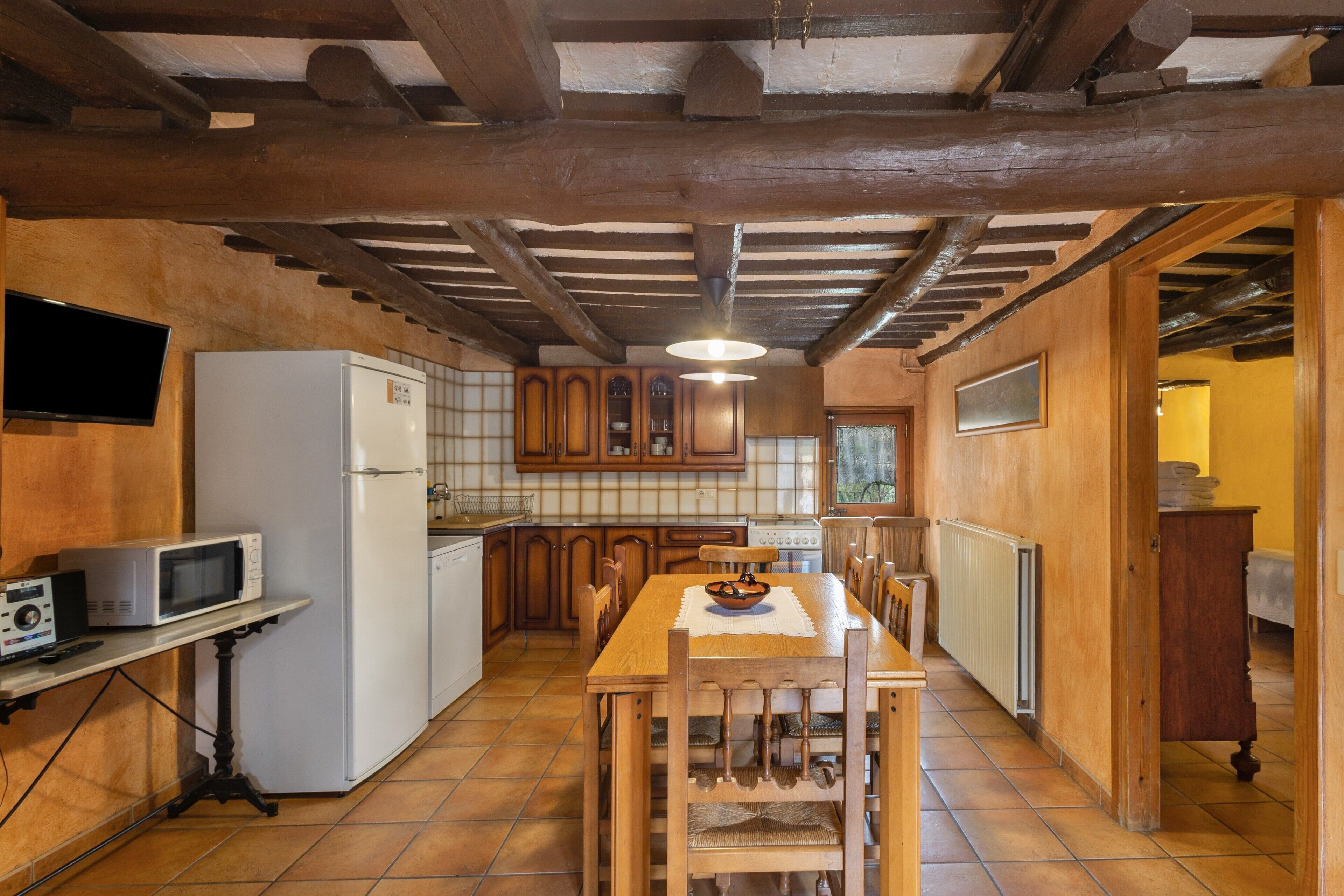 A kitchen with wooden cabinets, a dining table, chairs, a refrigerator, a microwave, and a television.