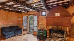 Un intérieur rustique avec un plafond en bois, une cheminée, un canapé et une porte donnant sur l’extérieur.