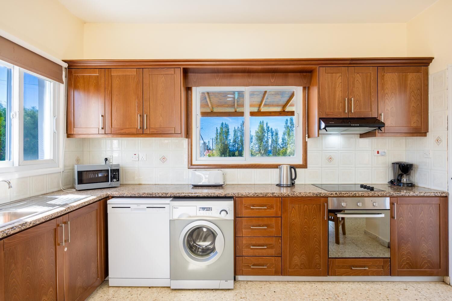 A compact kitchen with wooden cabinets, a built-in microwave, a dishwasher, a washing machine, and a stove.