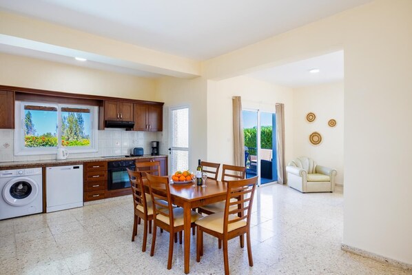 A modern kitchen with a dining area, a washing machine, and a sofa in a bright living space. - Villa Andreas - Two Bedroom Villa, Sleeps 4 (Argaka)