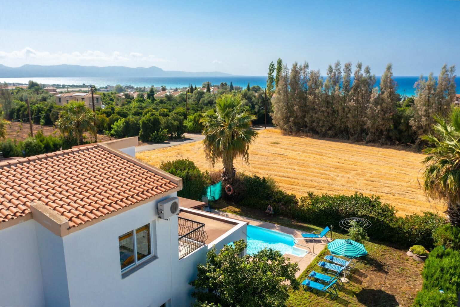 A residential property with a swimming pool, a view of the sea, and a large open field.