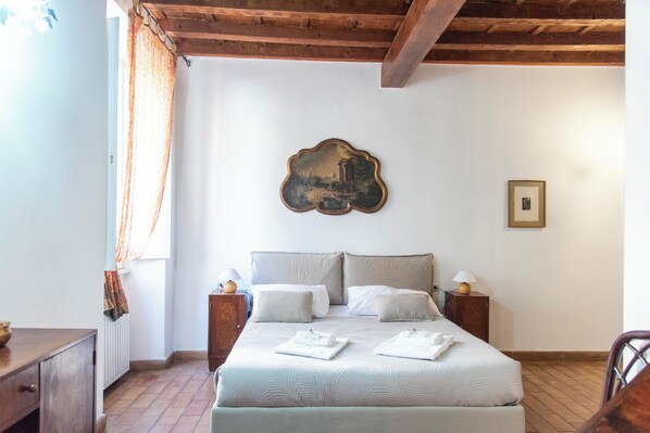 A bedroom with a bed, two bedside tables, a nightstand, a wooden headboard, a wall-mounted picture, and a window with curtains. - Jacopo Monti - 2 bedrooms with ansuite bathrooms (Roma)