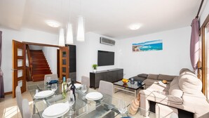 A modern living room with a glass dining table, a sofa, and a staircase leading to another level.