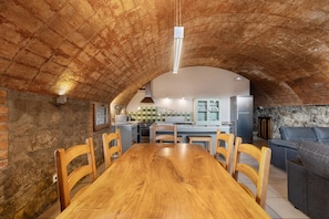 Un comedor con una mesa y sillas de madera, una cocina al fondo y una pared de piedra.