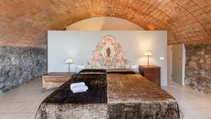 A room with a bed, stone walls, a decorative headboard, and two bedside lamps.