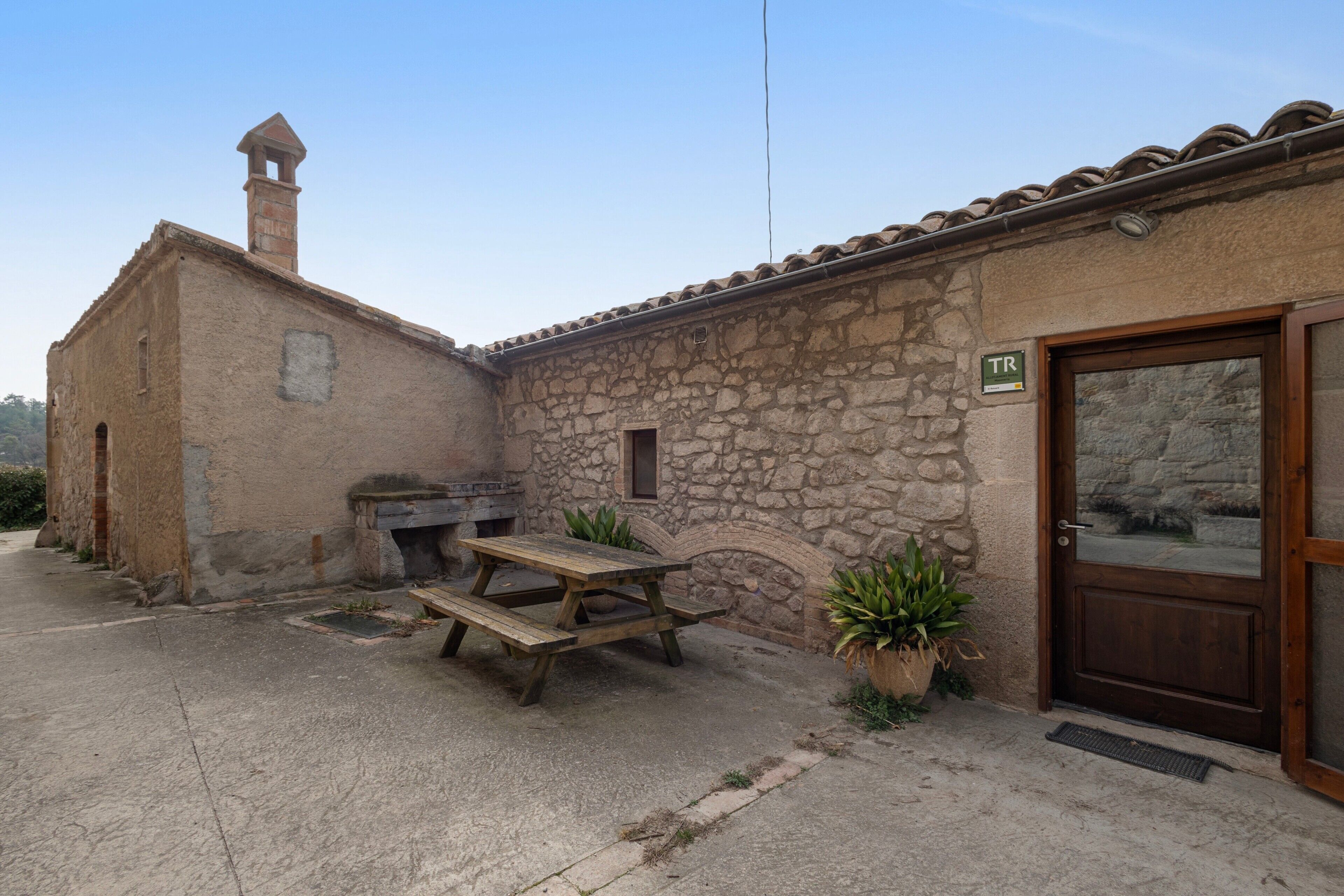 Un edificio rústico de piedra con puerta de madera, una mesa de picnic y una ventana pequeña.