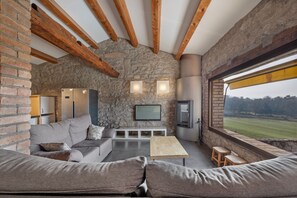 A modern living room with stone walls, wooden beams, a large window, and a built-in TV.