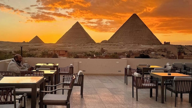 A rooftop terrace with tables and chairs, overlooking the pyramids during sunset.