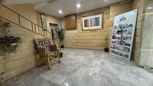 A lobby with a marble floor, a staircase, a wooden wall panel, a framed picture, a decorative table, and a poster advertising tours. - Sands of Majesty (Al Haram)