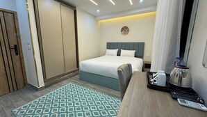Habitación de hotel con cama, escritorio con bandeja de artículos de aseo y tetera incorporada a la pared.