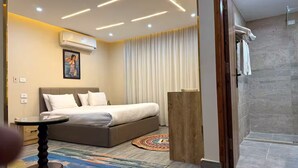 A modern hotel room with a bed, bedside table, and a shower area. - Pyramid Royals (Al Haram)