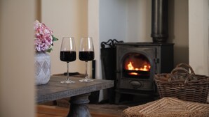 A cozy room with a fireplace, a table with two glasses of red wine, and a woven basket.