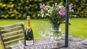 A bottle of champagne, four glasses, and a floral arrangement on a wooden table.