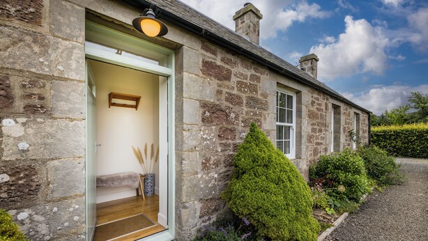 A stone building with a wooden door and steps leading to a bench inside.